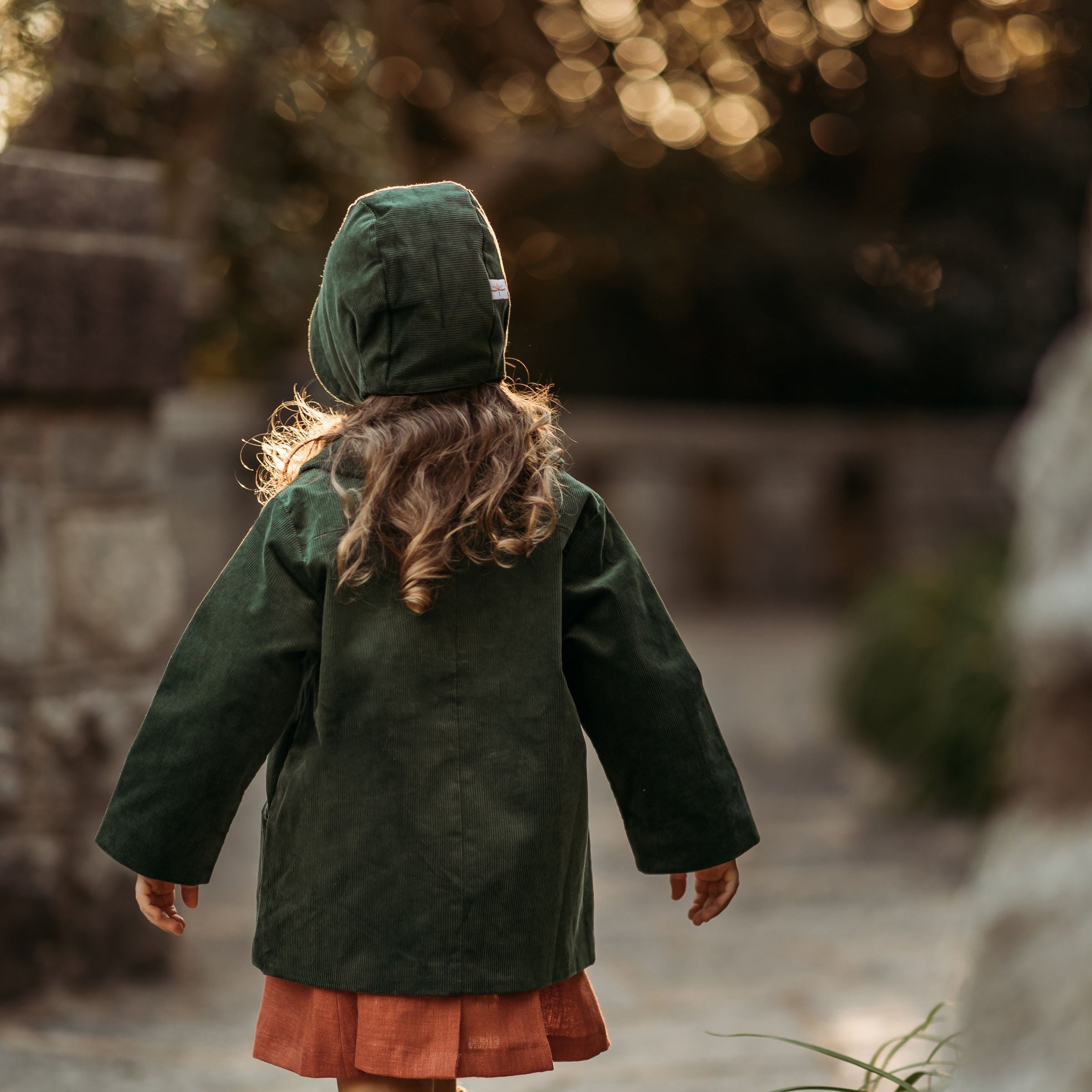 Back view of the girl in the Evergreen bonnet and matching coat, highlighting the quality and durability of sustainable children’s wear for hand-me-downs.