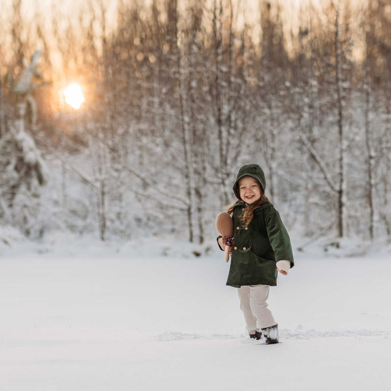 Three-year-old girl in a white, snowy field wearing the Evergreen bonnet and matching corduroy coat, epitomizing natural, eco-friendly fashion for kids.