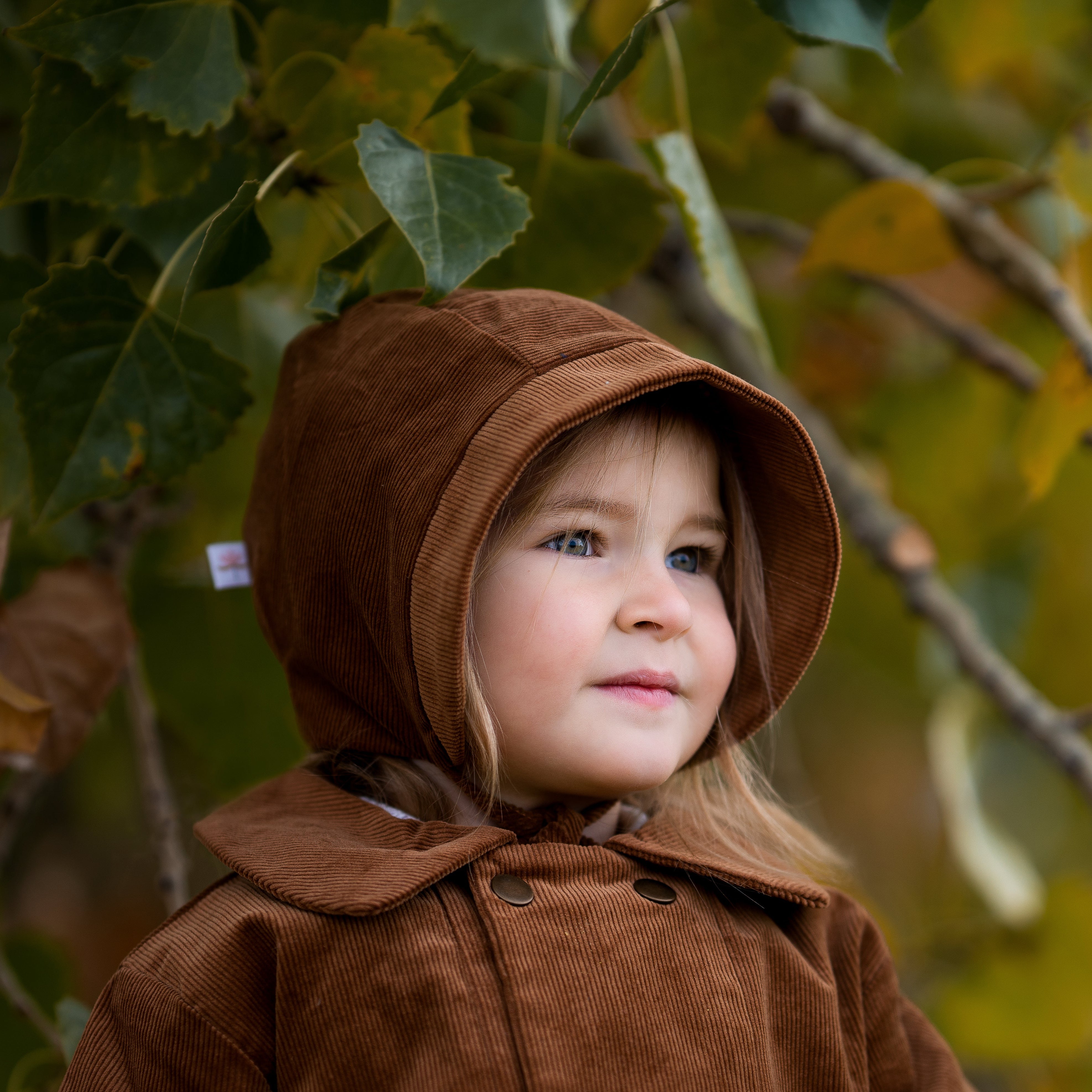 Model girl wearing the Camel Bonnet, detail view - This close-up shot focuses on the bonnet’s fabric and lining, emphasizing the coordinating brushed gingham cotton that adds comfort and warmth.