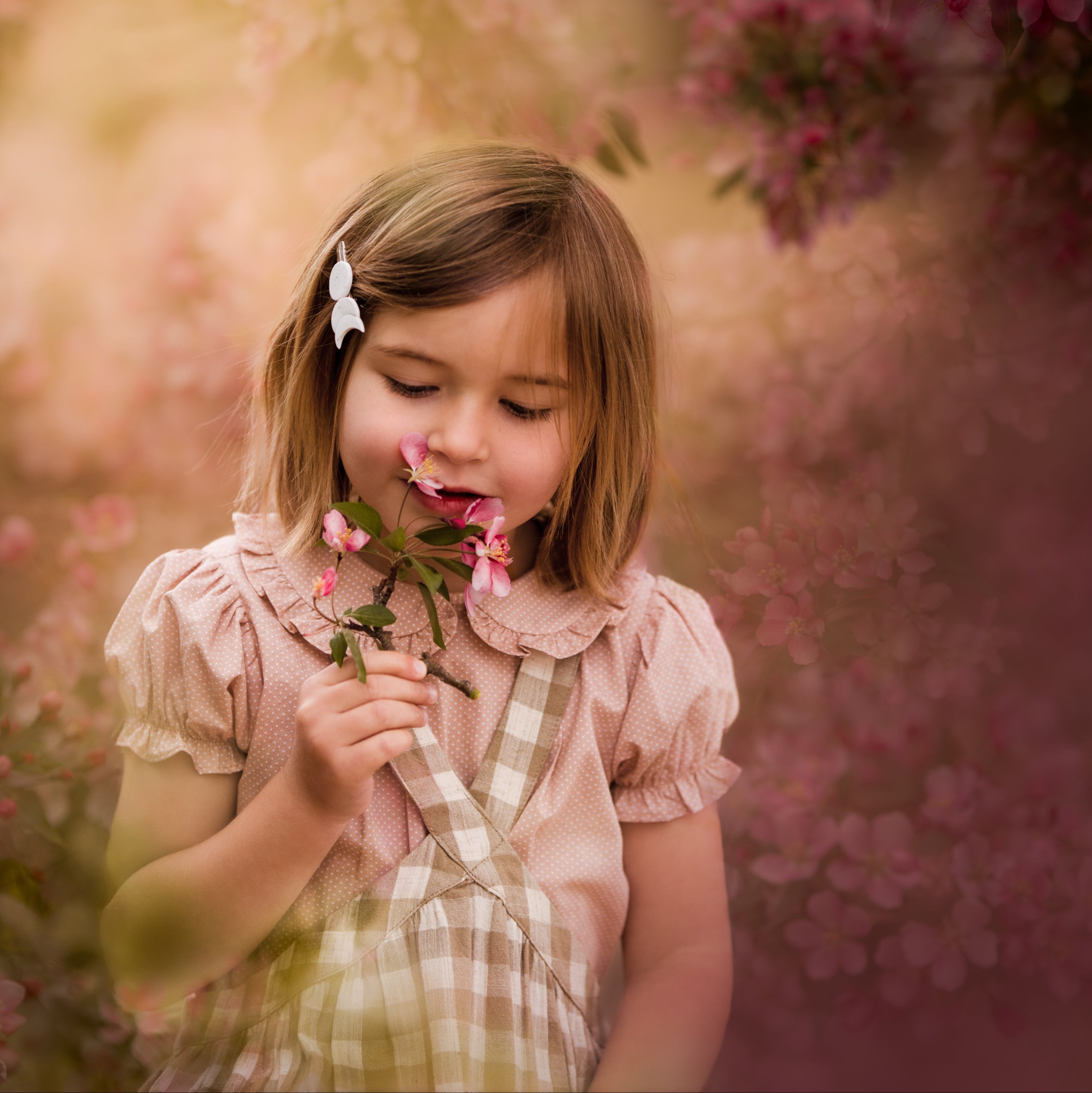 Detail of young girl wearing a beige blouse with white Swiss dots and a matching beige gingham pinafore. The blouse features a Peter Pan collar with ruffles and short puffy sleeves, while the pinafore showcases a classic gingham pattern, perfect for playful outfits.