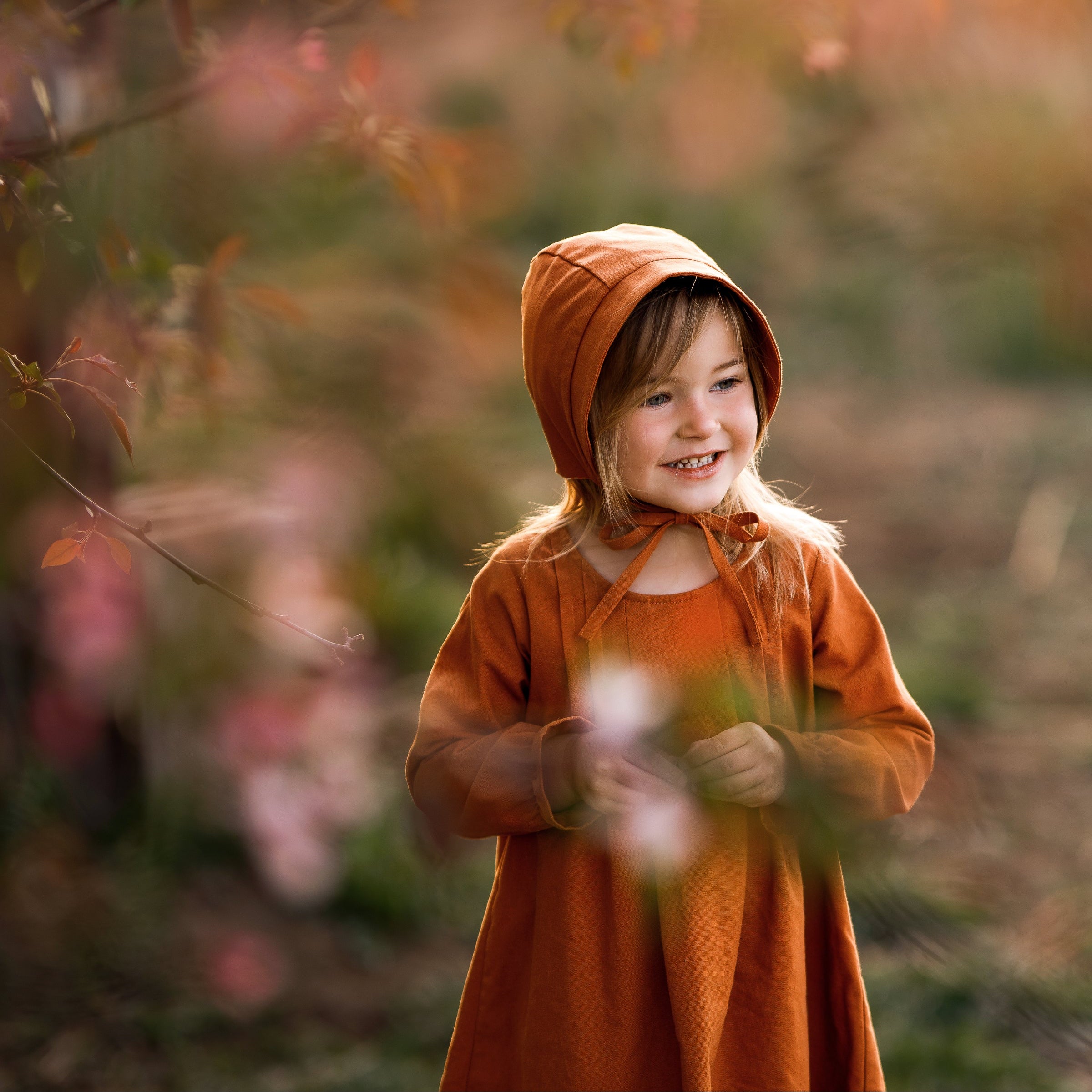 Girl in matching rust dress and bonnet smiling dreamily