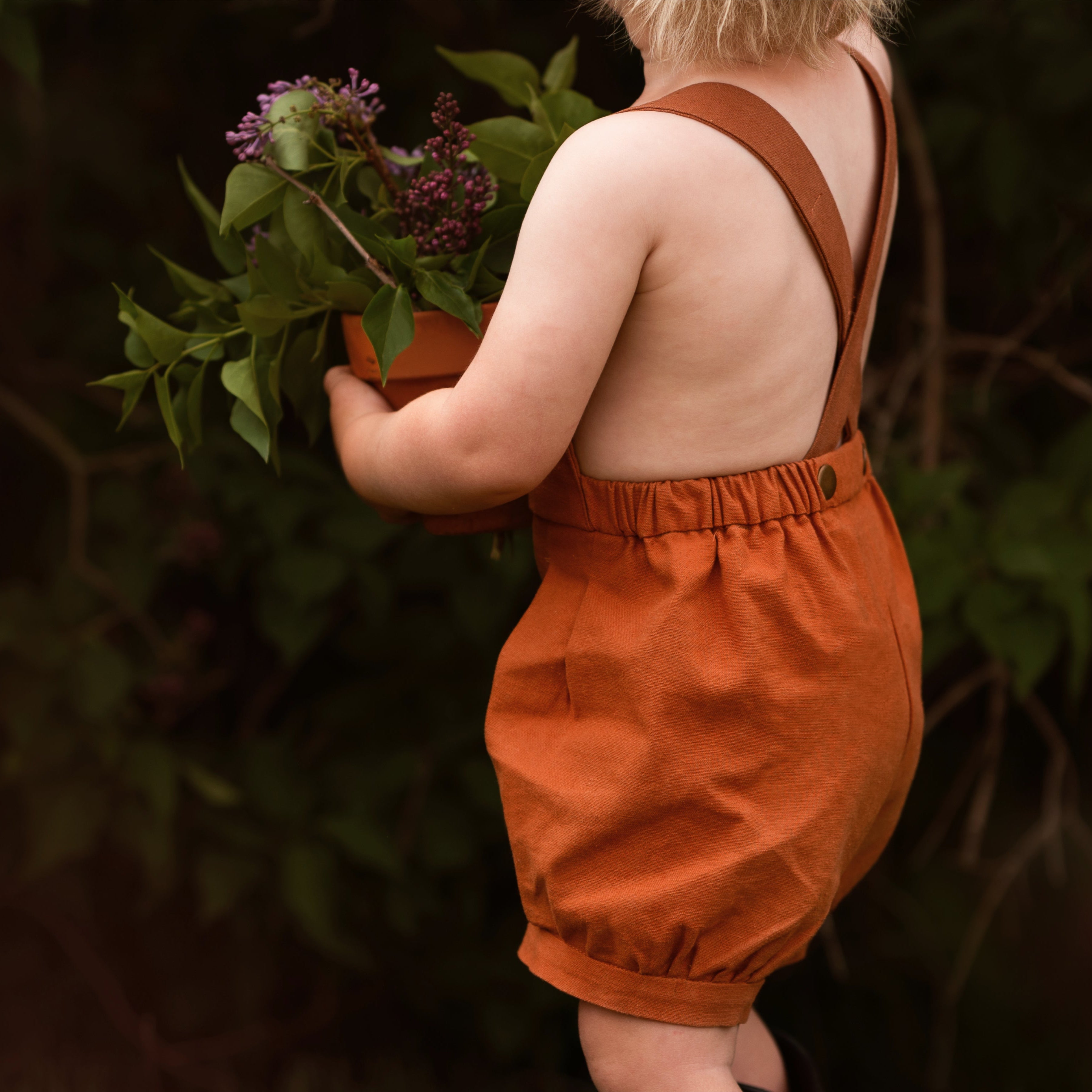 Back view of model boy playing outdoors in Burnt Orange Short Overalls - This image captures another playful moment, emphasizing the overall functionality and stylish appeal of the shortalls for active kids.