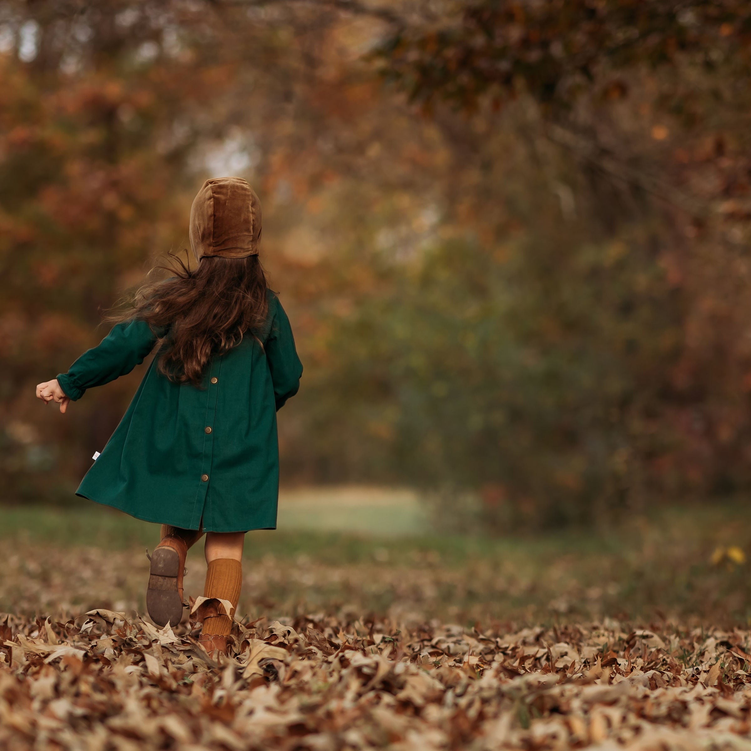 Back view of a 4-year-old girl running in the evergreen linen dress, illustrating the pleated back yoke that provides comfort and a stylish fit for active play.