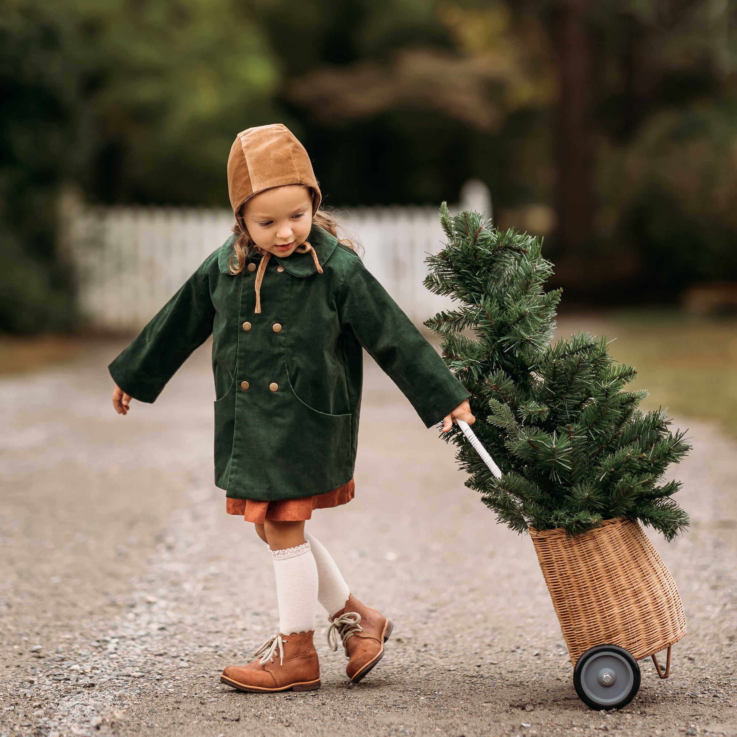 Model girl wearing the Gold Velvet Bonnet combined with our Evergreen Corduroy Coat, joyfully pulling a Christmas tree, showcasing the versatile design suitable for festive occasions.