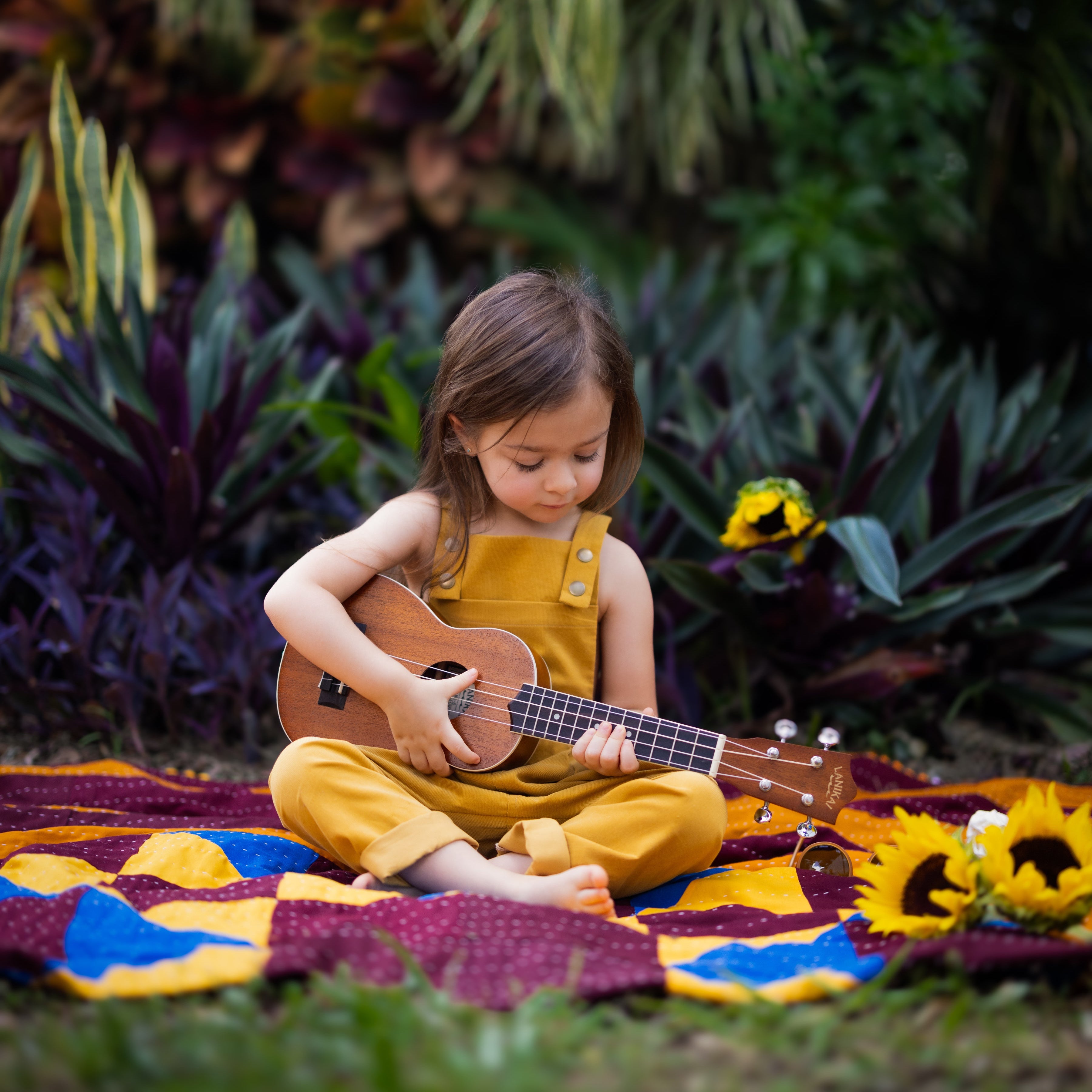 A 4-year-old girl playing ukulele freely in ginger long overalls, emphasizing the comfort and durability of the handmade 100% cotton fabric.