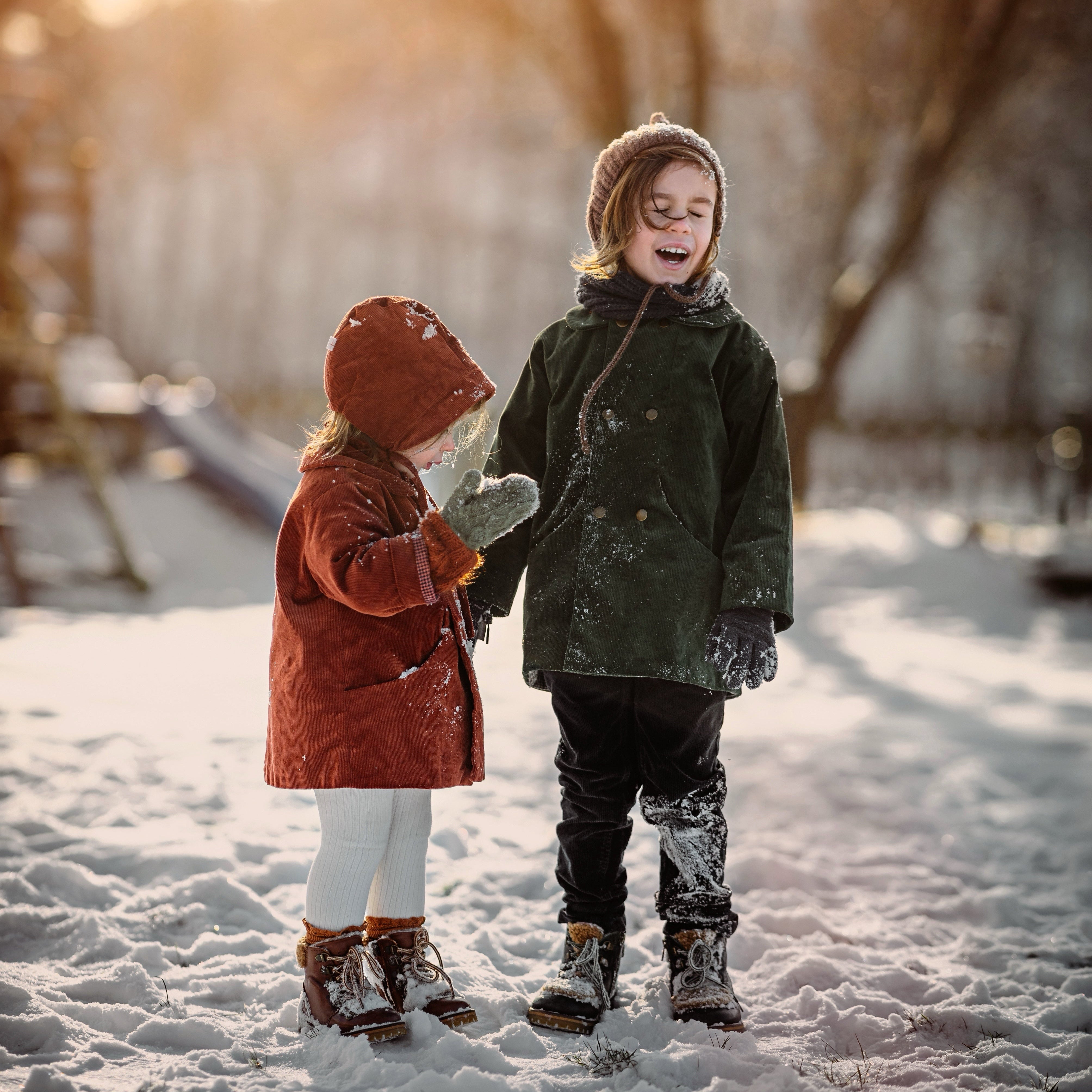 Boy and girl in matching green and rust coats in the snow smiling
