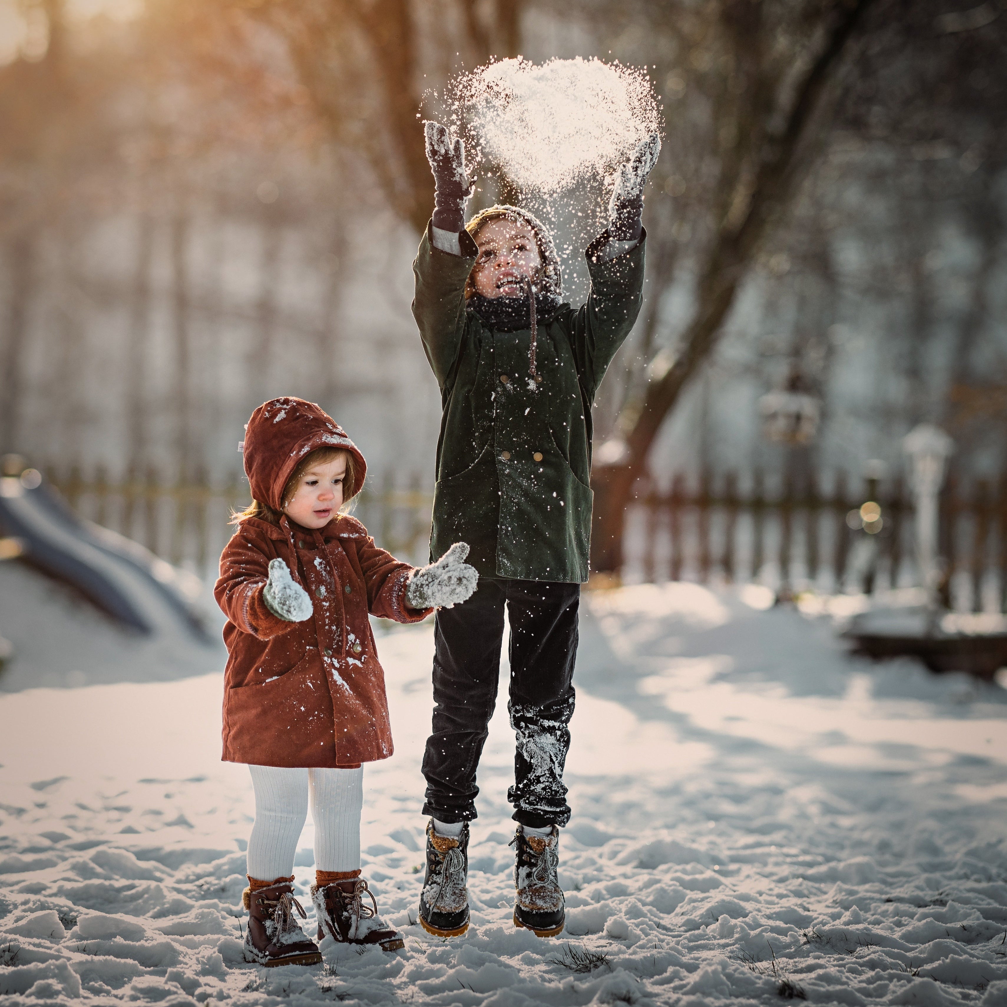 Boy and girl in matching green and rust coats playing in the snow
