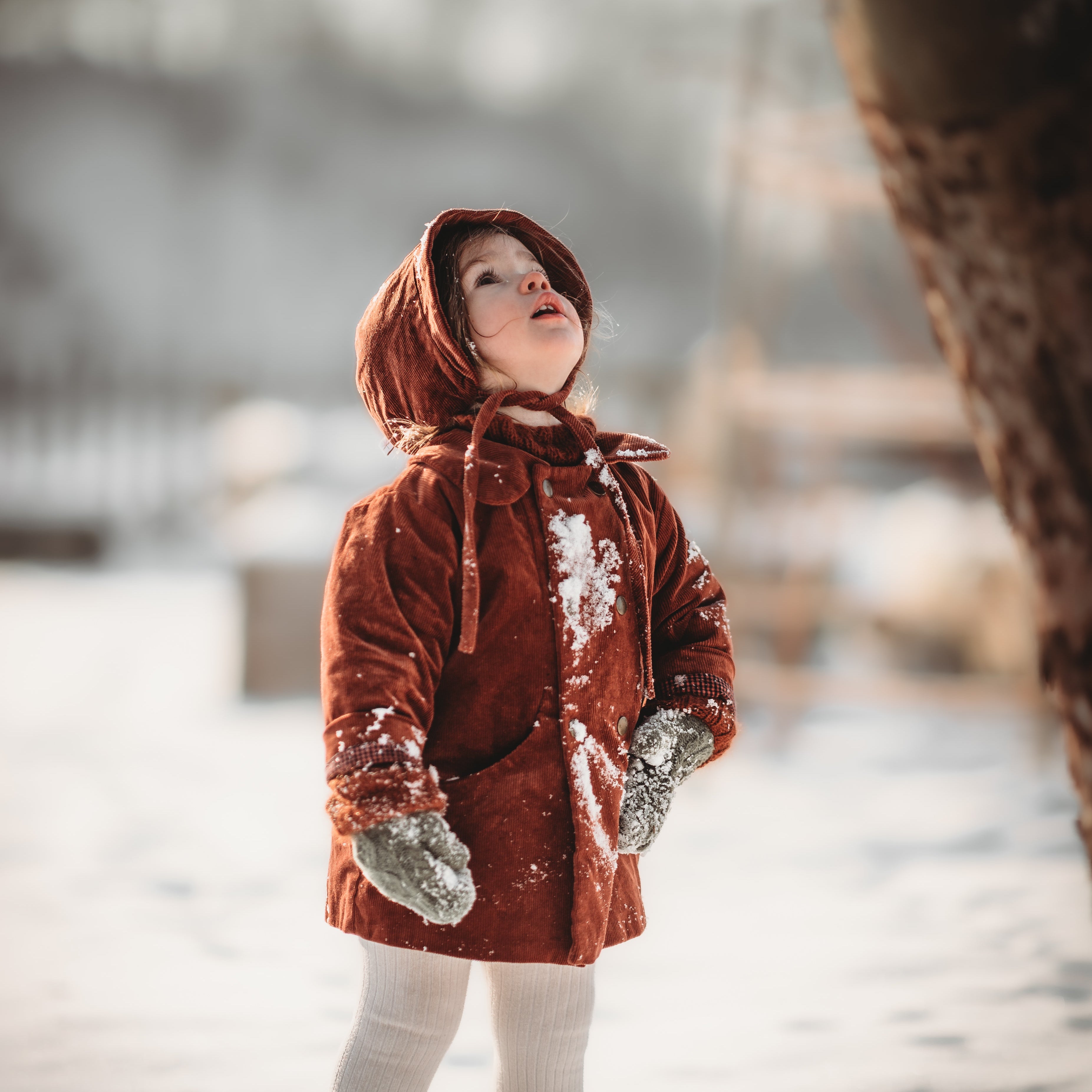Little girl in the snow in a rust coat and matching hat looking up