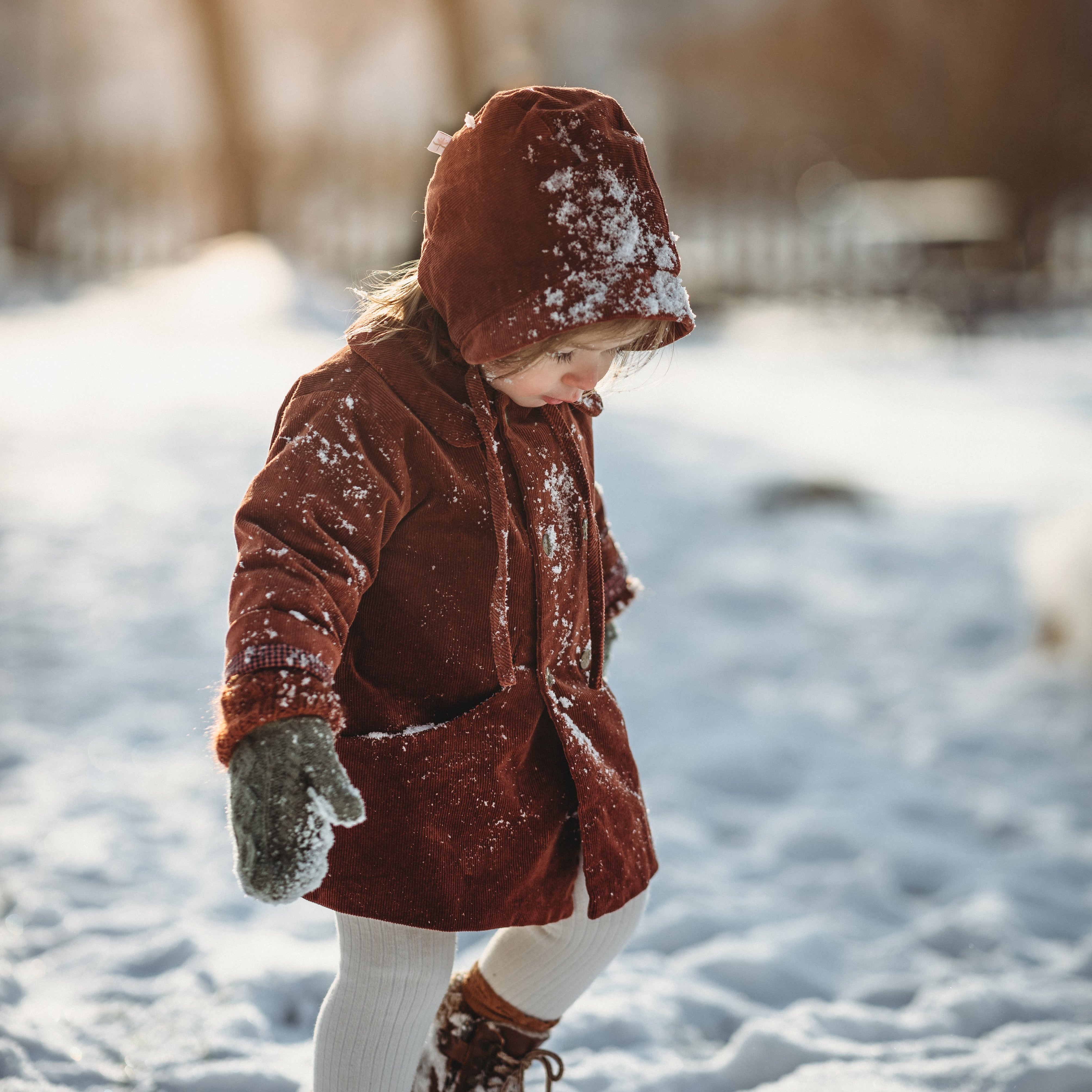Little girl in the snow in a rust coat and matching hat