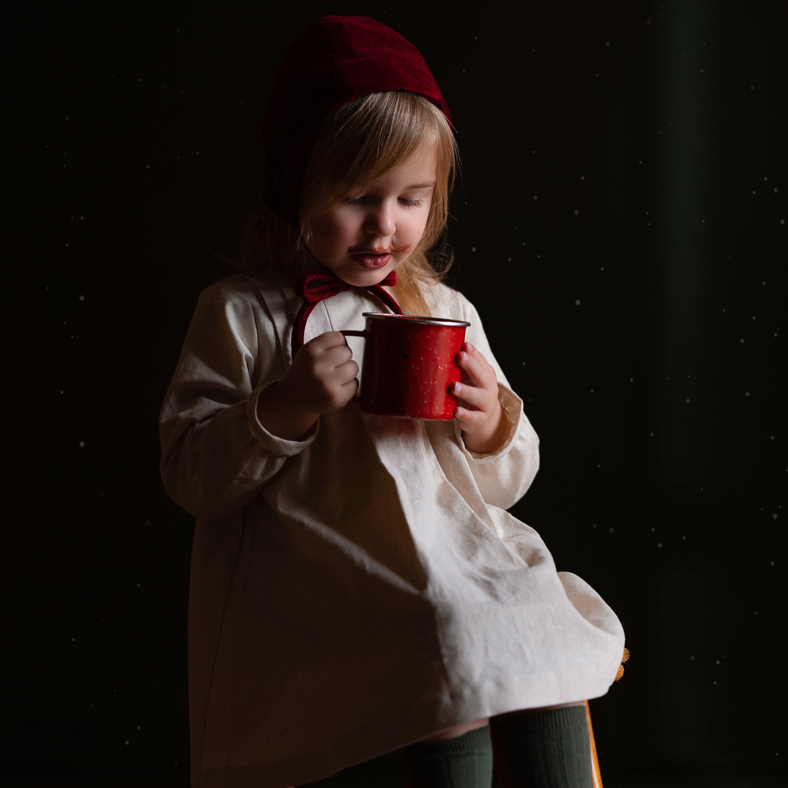 Child holding a red mug in a dark setting