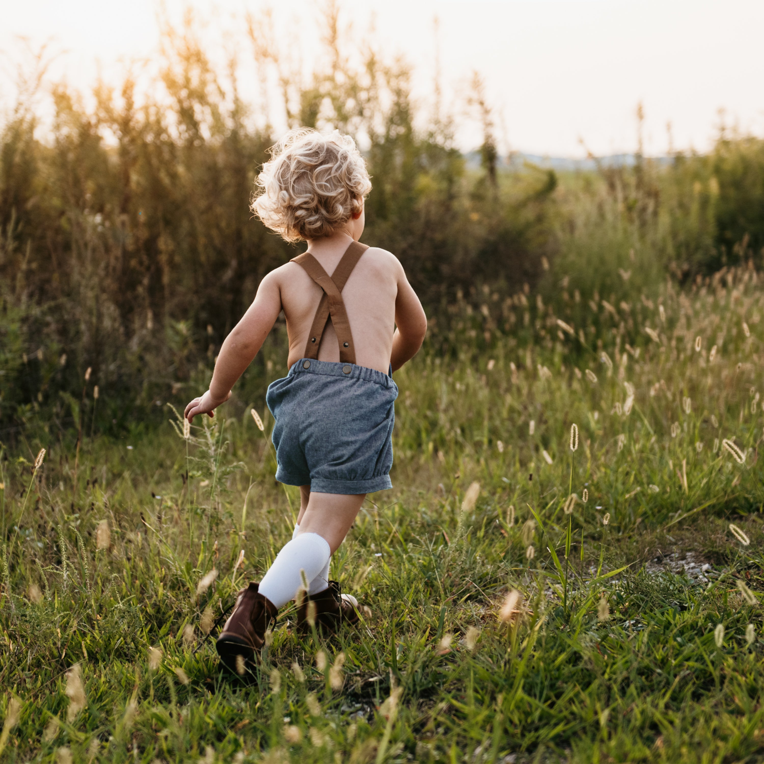 A playful 3-year-old boy running in chambray blue linen short overalls, showcasing the stylish design and comfort in action, perfect for playdates and family gatherings