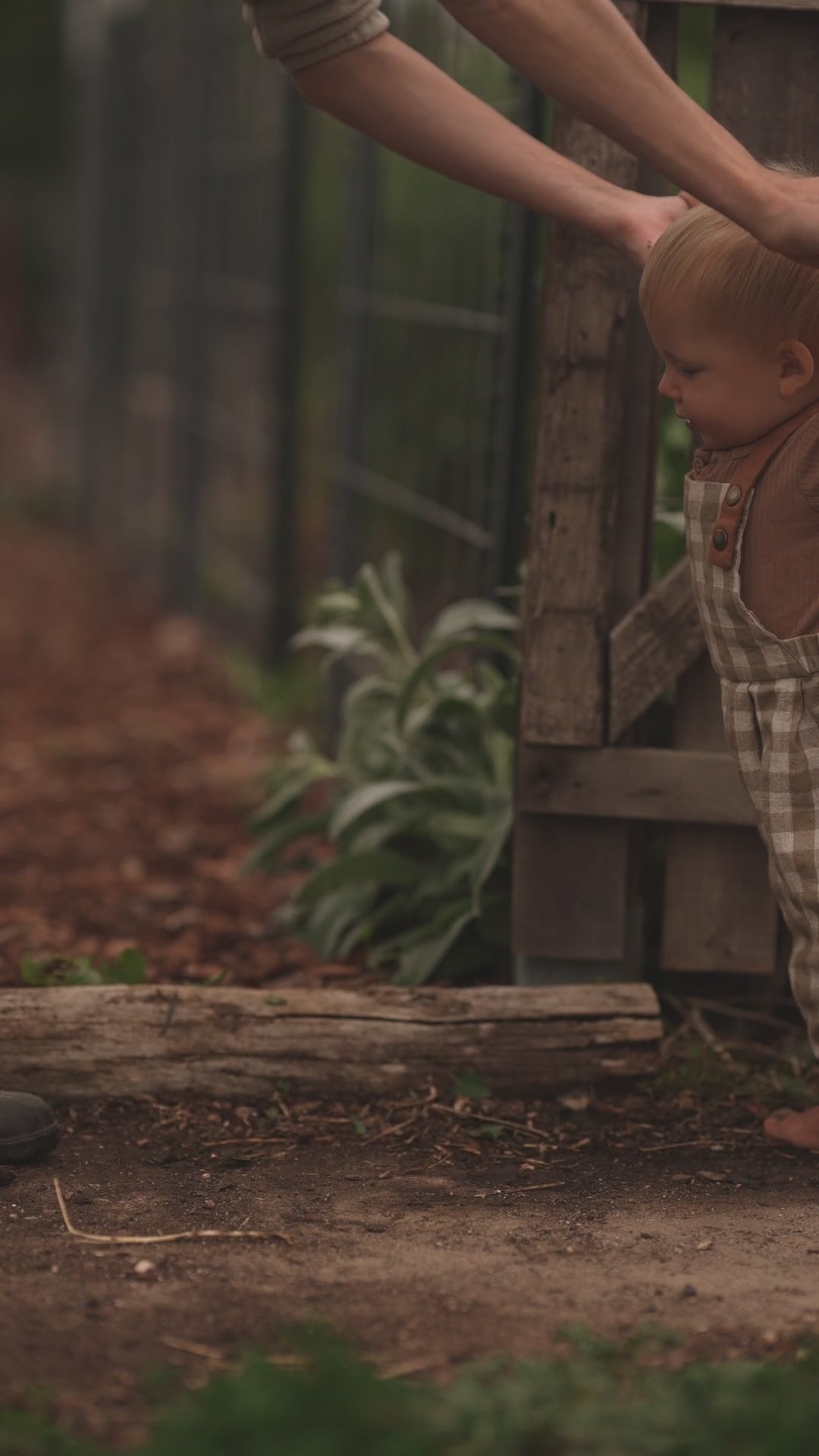 Baby learning to walk in beige gingham linen overalls, showcasing the comfortable and breathable fabric, adjustable straps for a perfect fit, and unfoldable leg cuffs designed to accommodate growth.