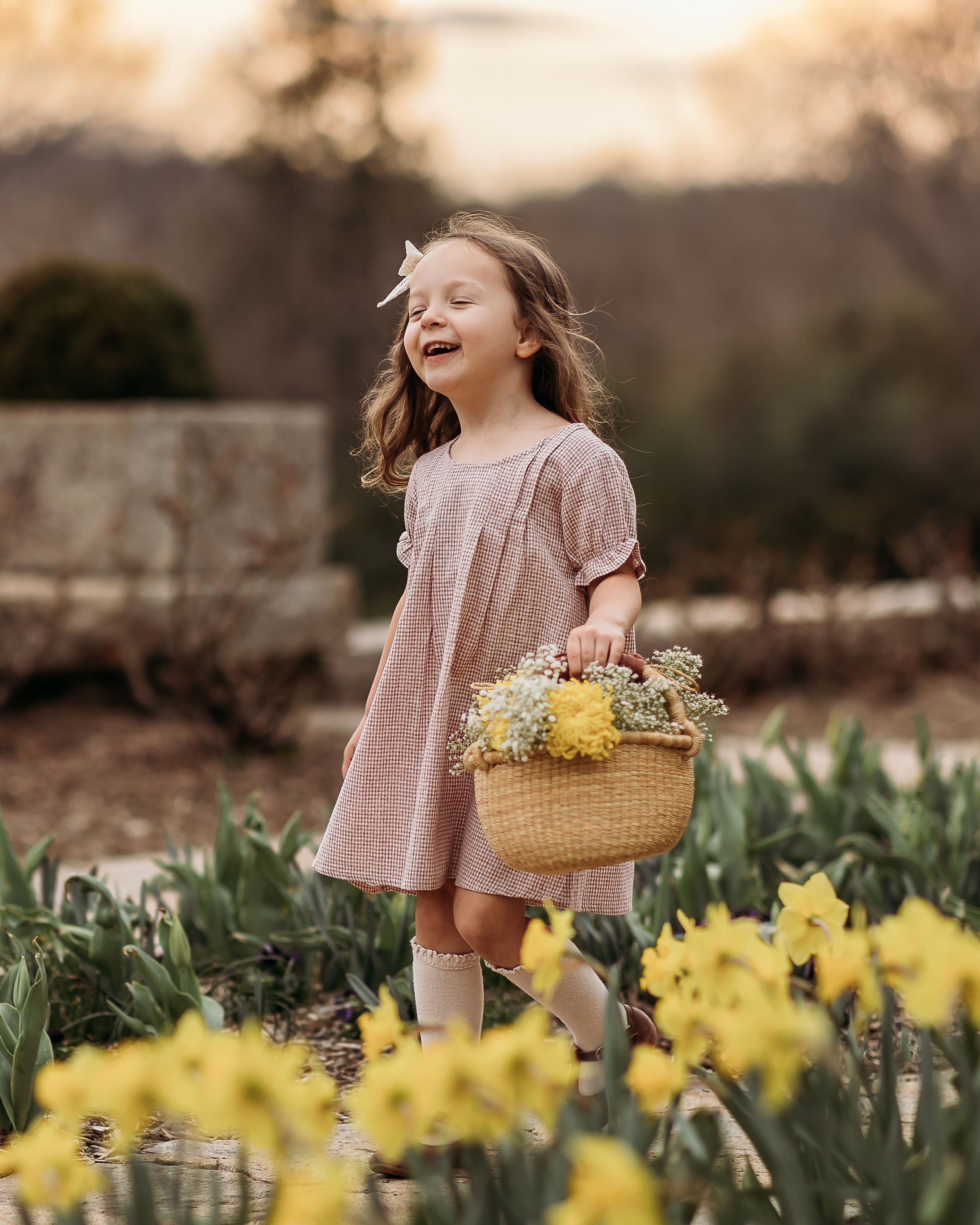 Young girl in a pink dress holding a basket of flowers in a field of yellow tulips.