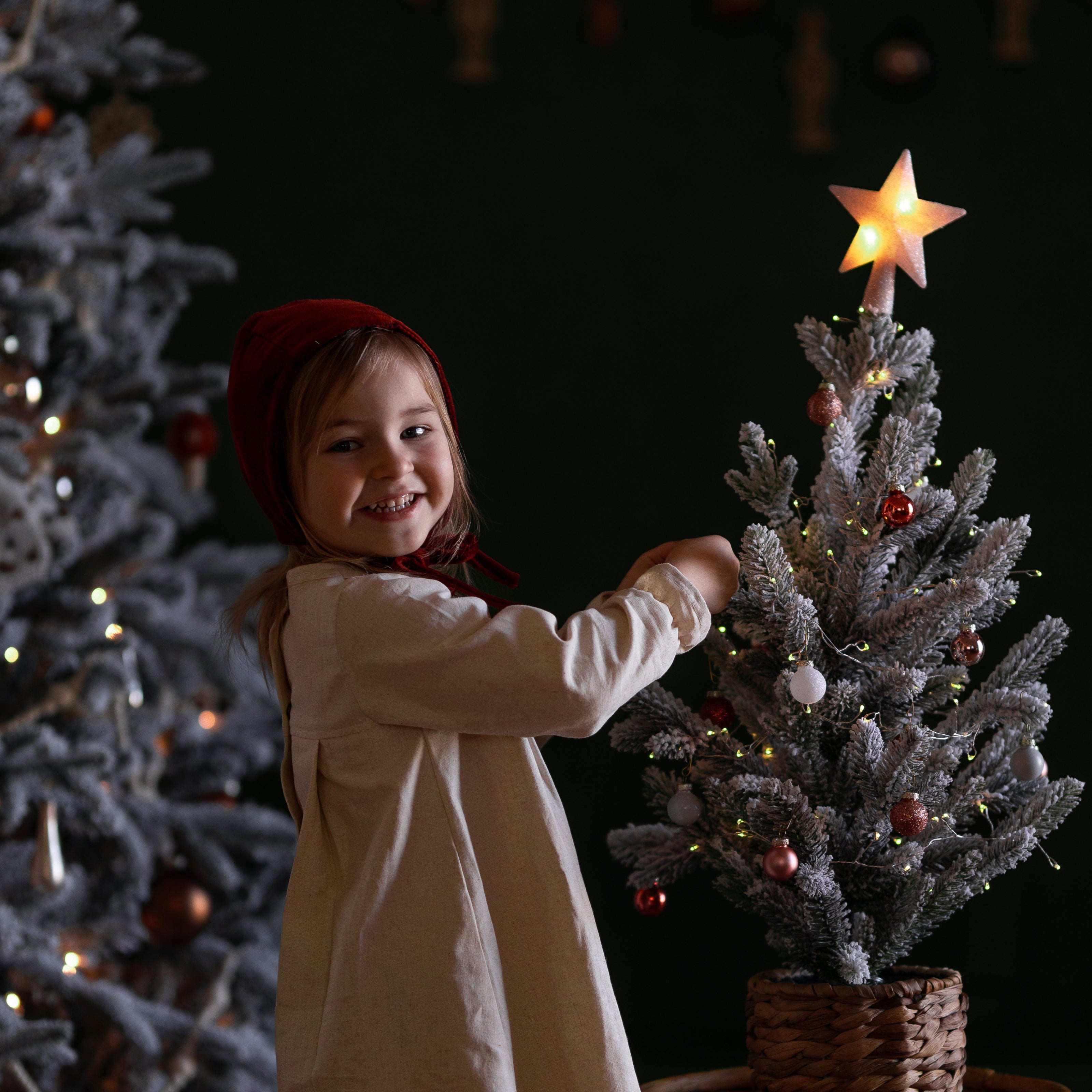 Child decorating a small Christmas tree with a star ornament against a dark background