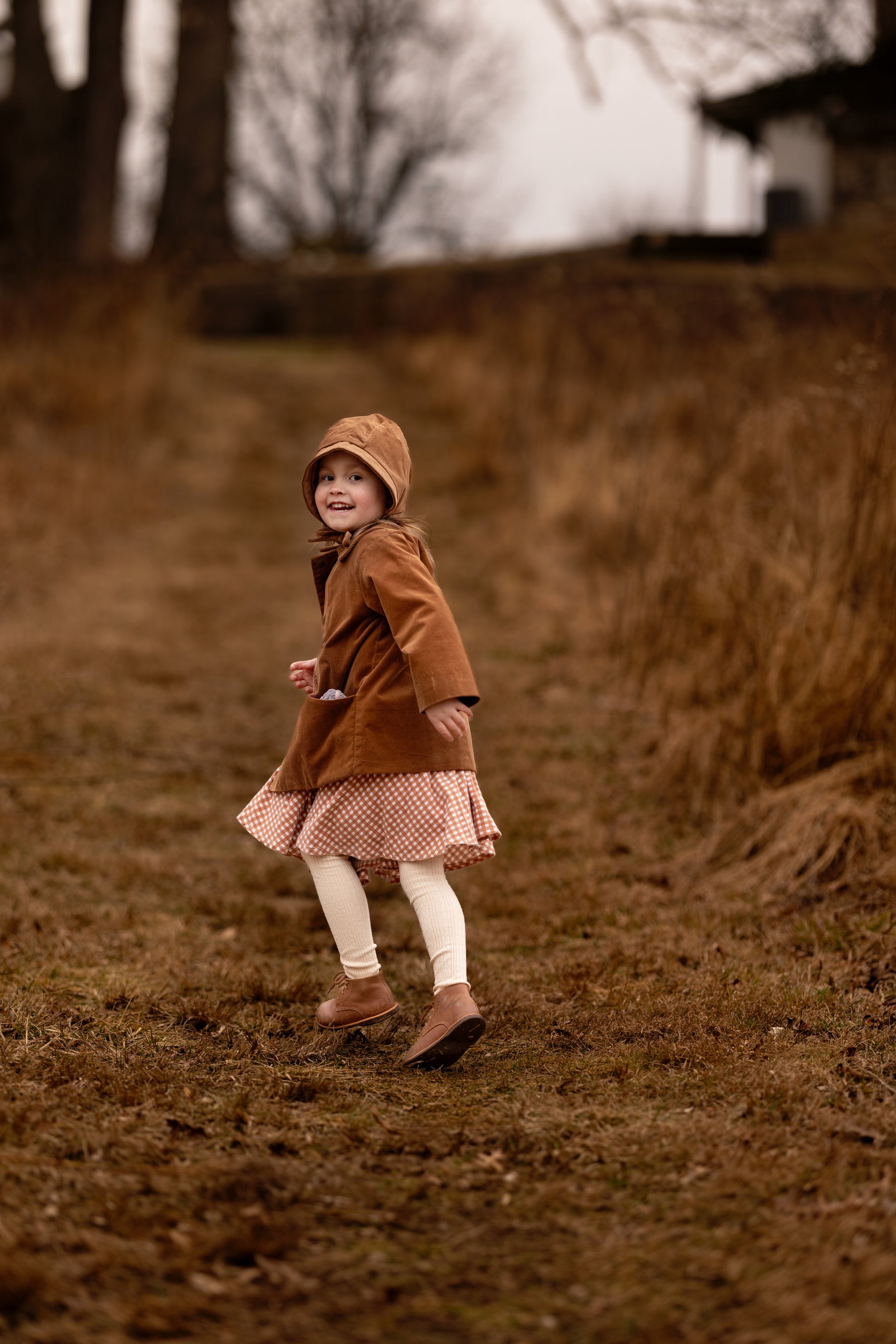 Child in a brown coat standing in a field with trees in the background