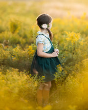 Young girl in a green dress standing in a field of yellow flowers.
