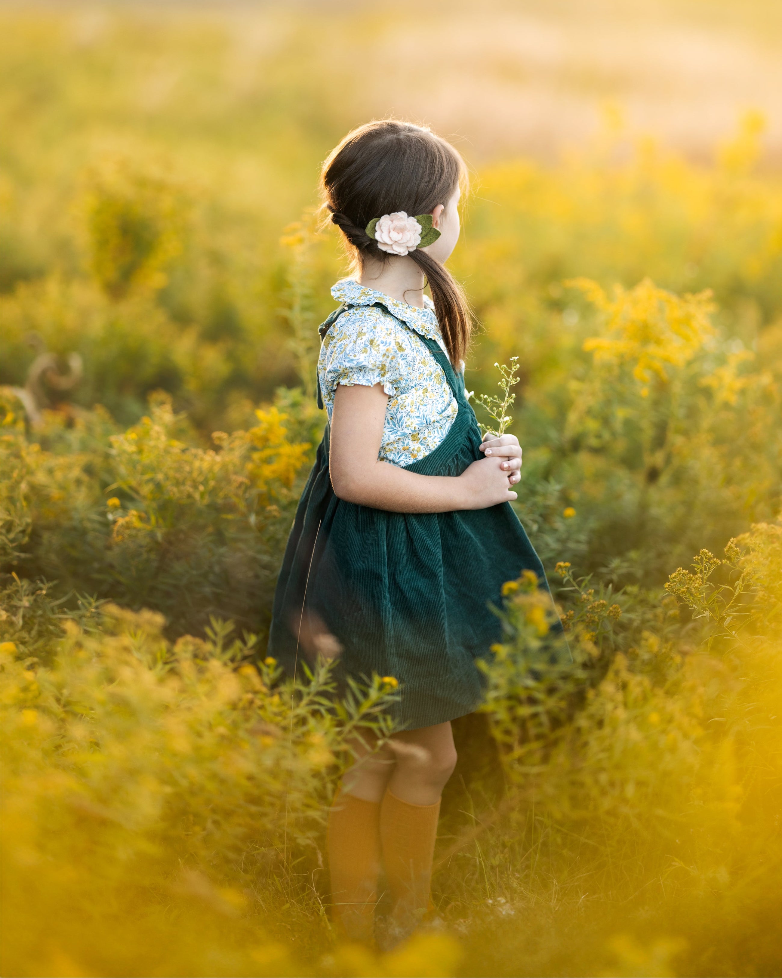 Young girl in a green dress standing in a field of yellow flowers.