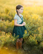 Young girl in a green dress standing in a field of yellow flowers.