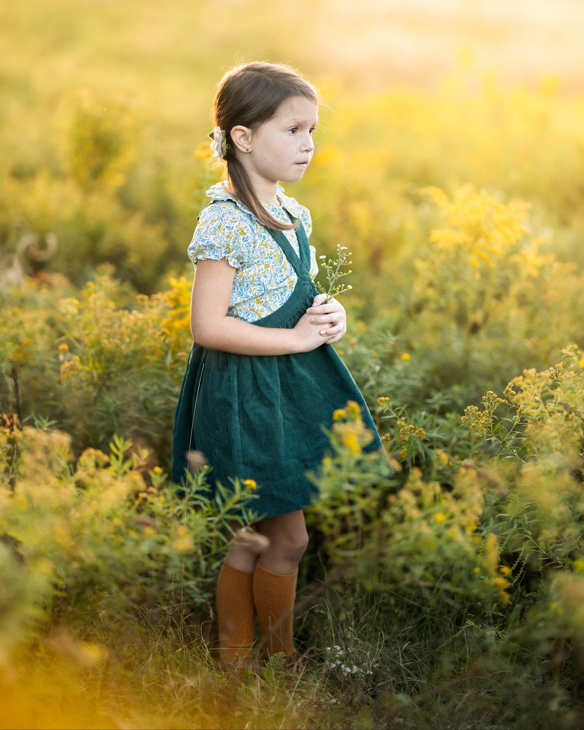 Young girl in a green dress standing in a field of yellow flowers.