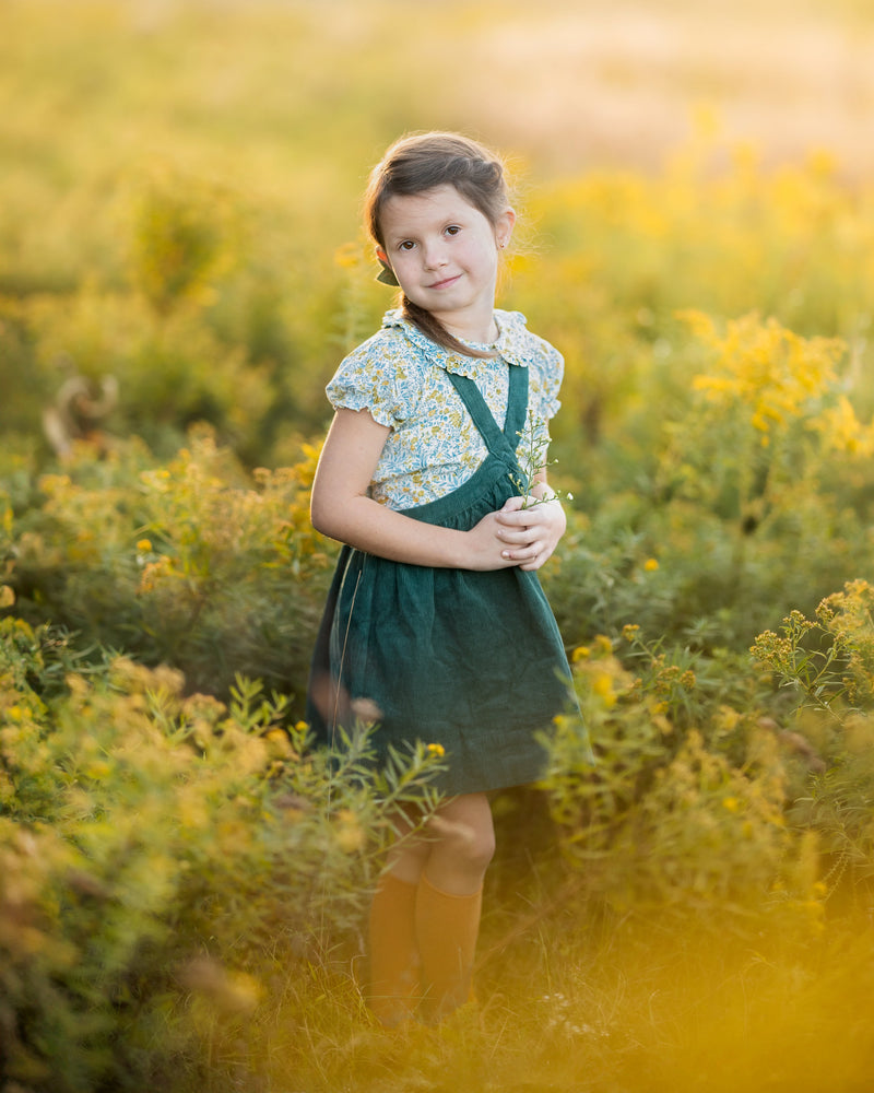 Young girl in a green dress standing in a field of yellow flowers