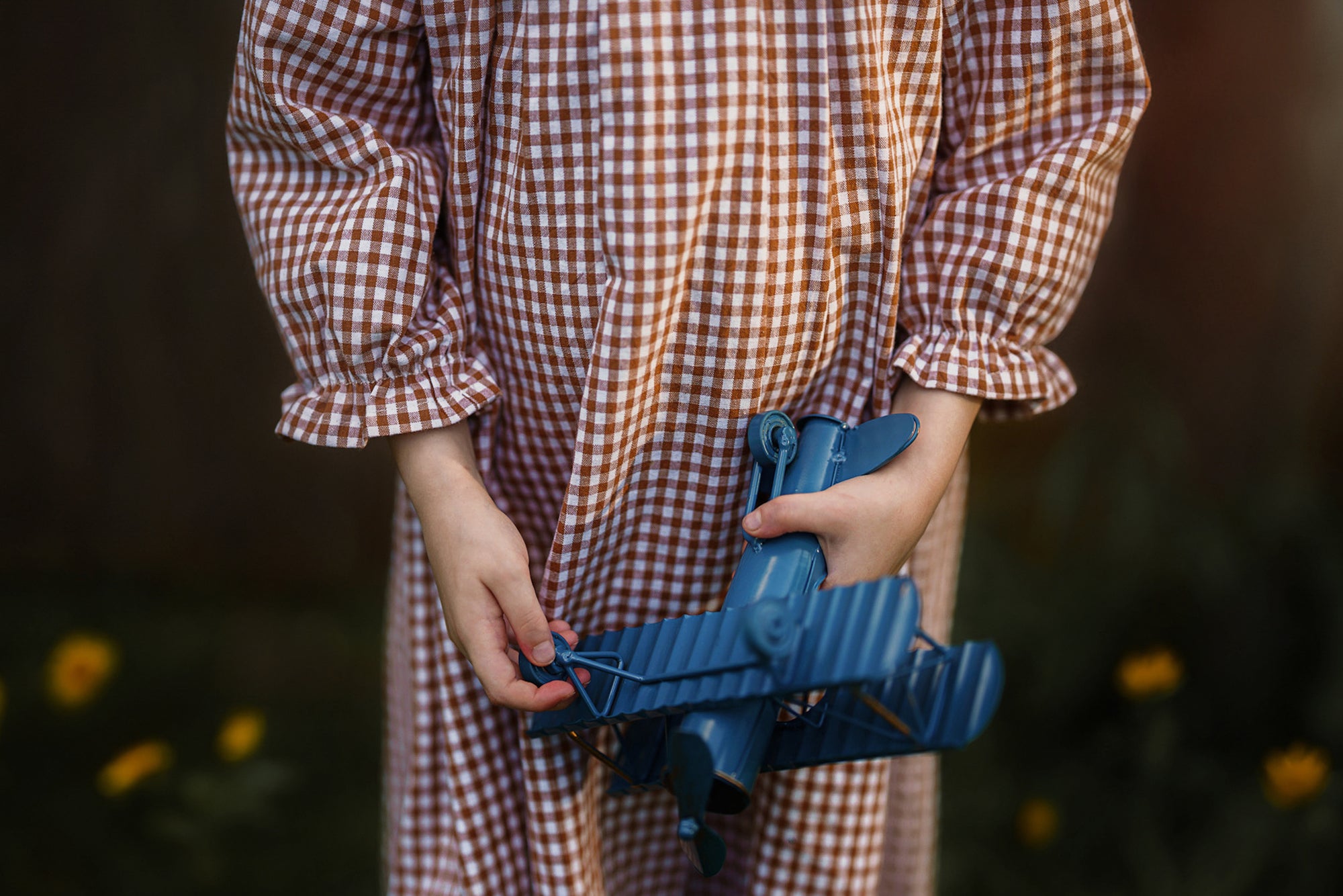 Person wearing a checkered outfit holding a blue object against a blurred natural background
