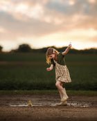 Child playing in a muddy puddle with a duckling at sunset.