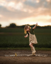 Child playing in a muddy puddle with a duckling at sunset.