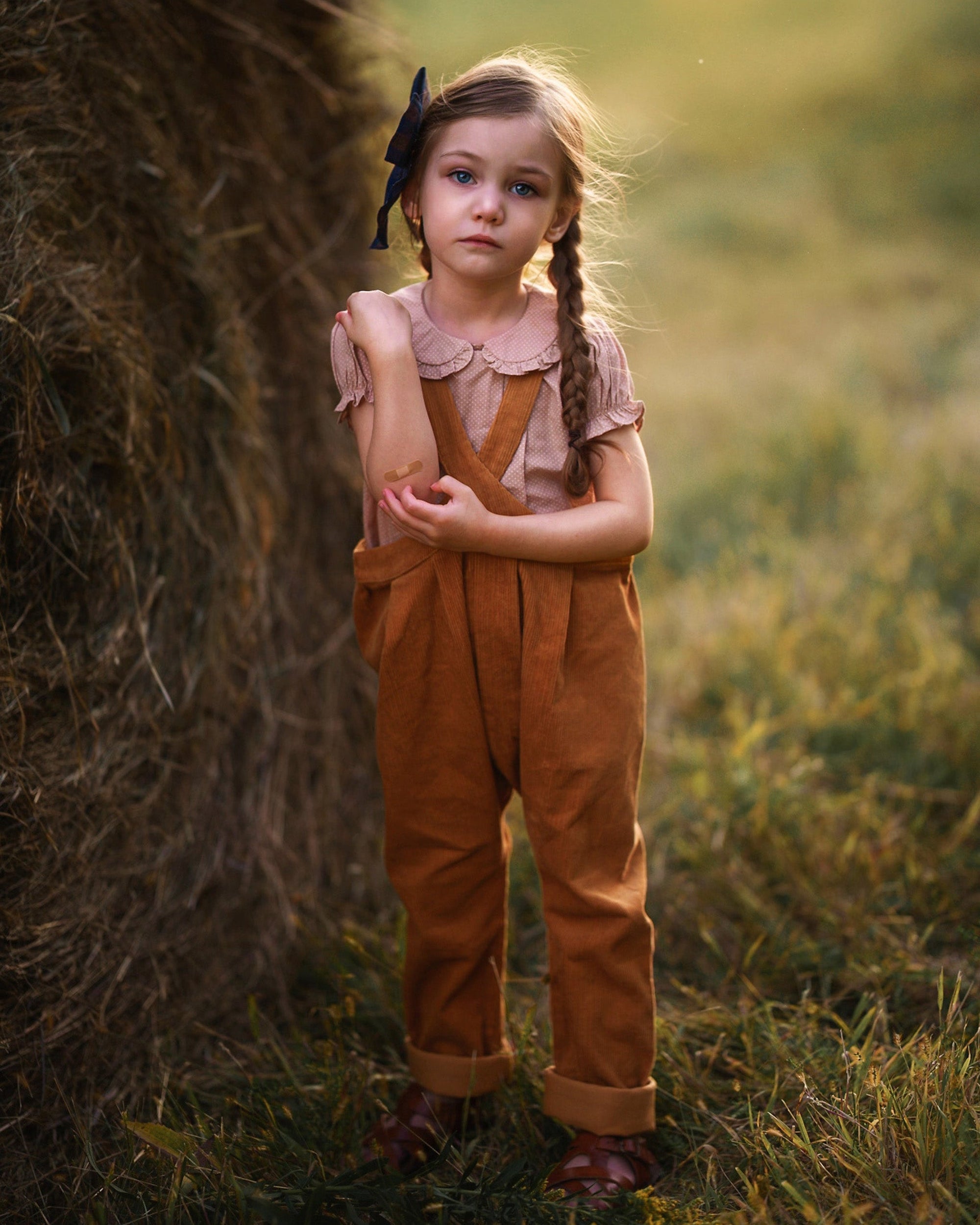 Young girl in a field wearing a brown outfit with a bow in her hair.