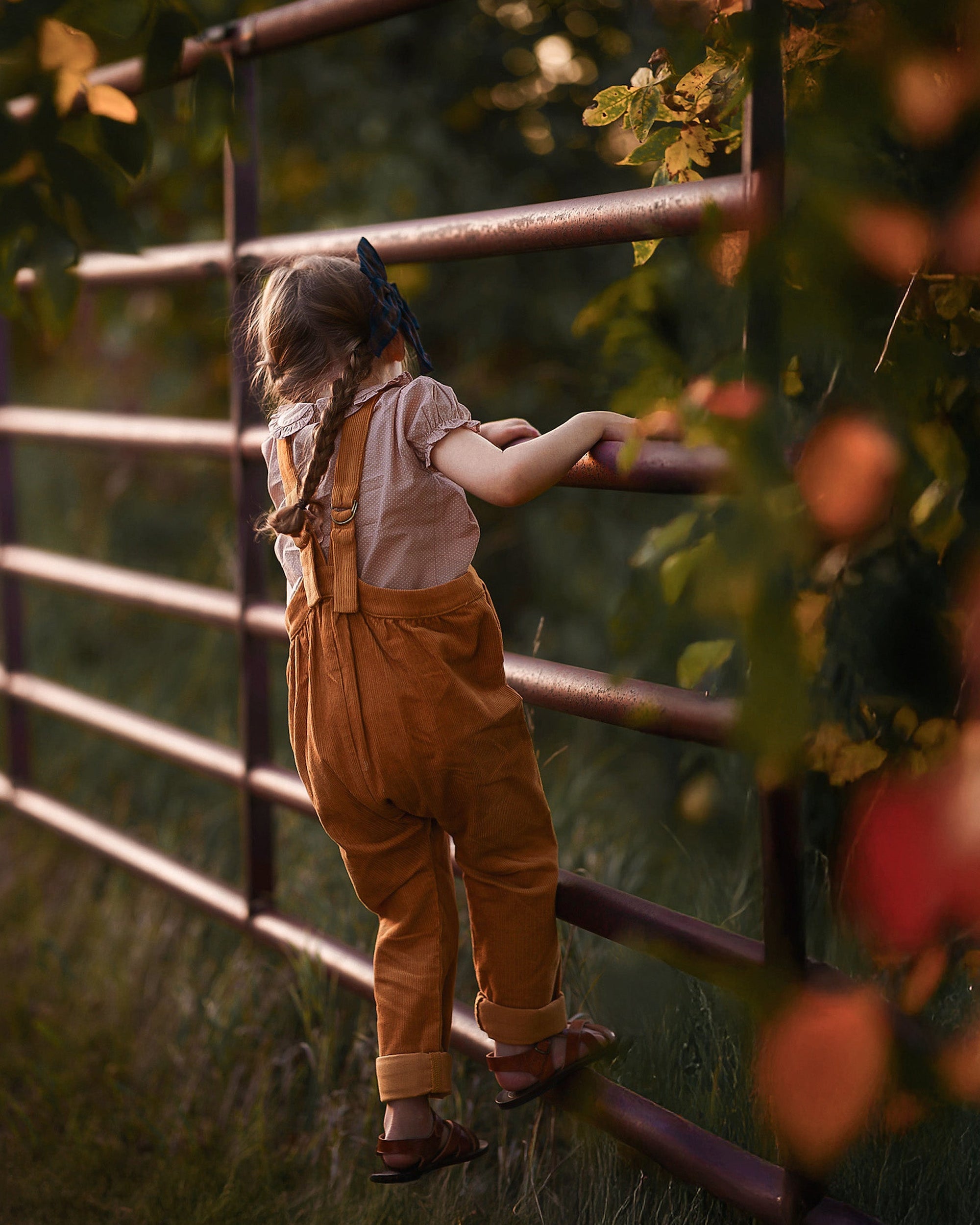 Child standing behind a metal fence with greenery in the background