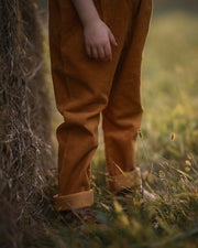 Girl wearing brown pants standing in a grassy field with a blurred background