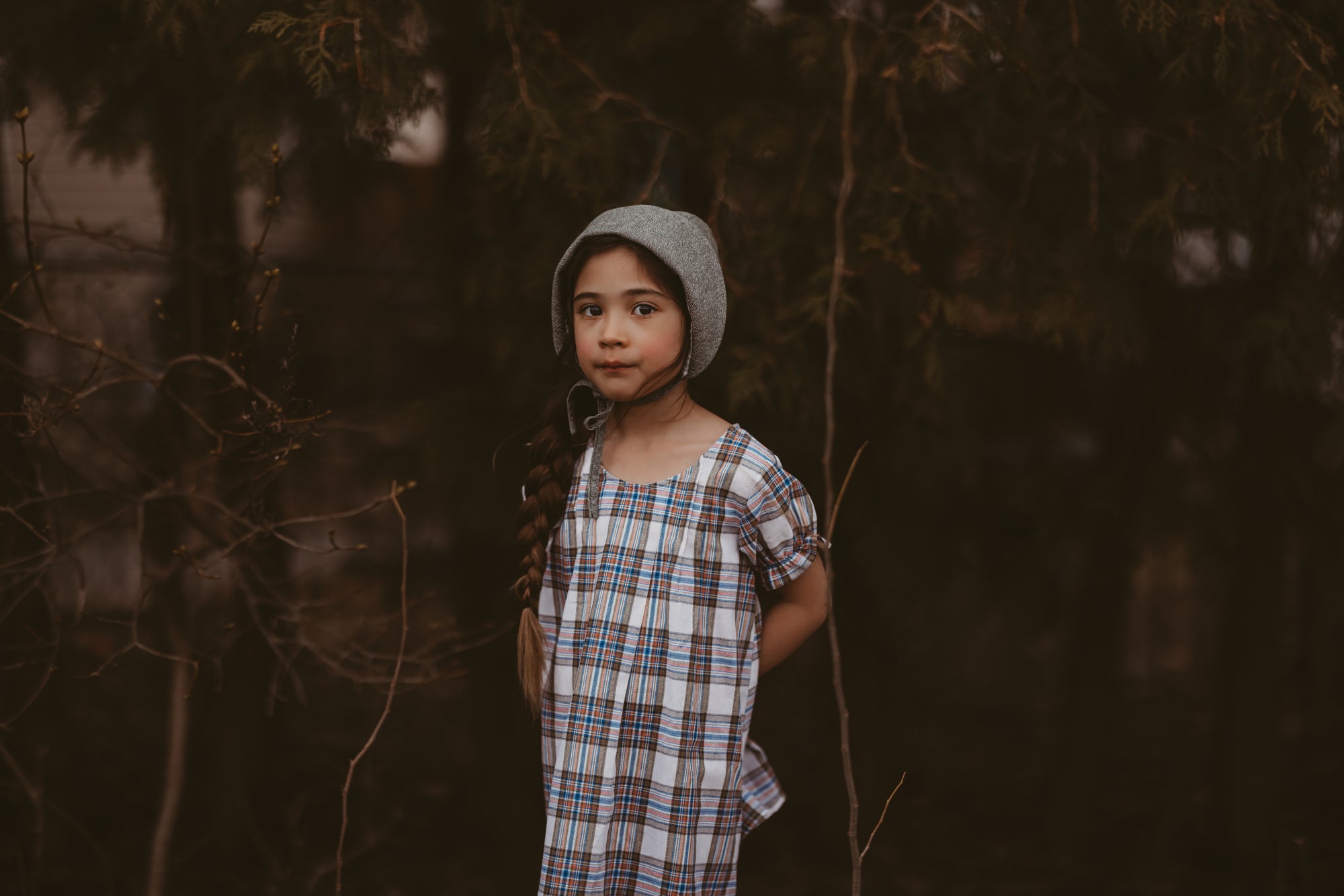 Girl in a plaid dress and green bonnet in a forest