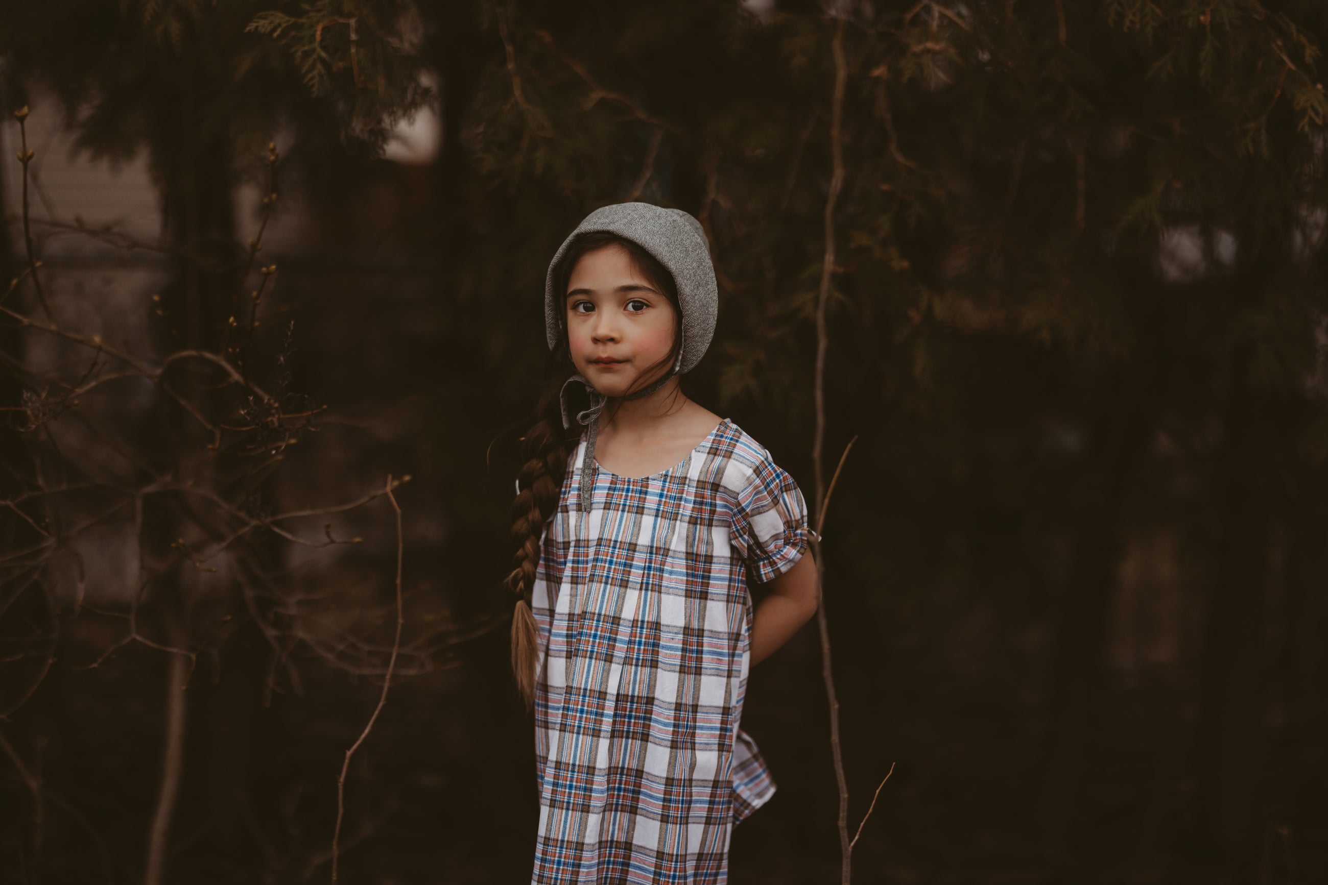 Girl in a plaid dress and green bonnet in a forest