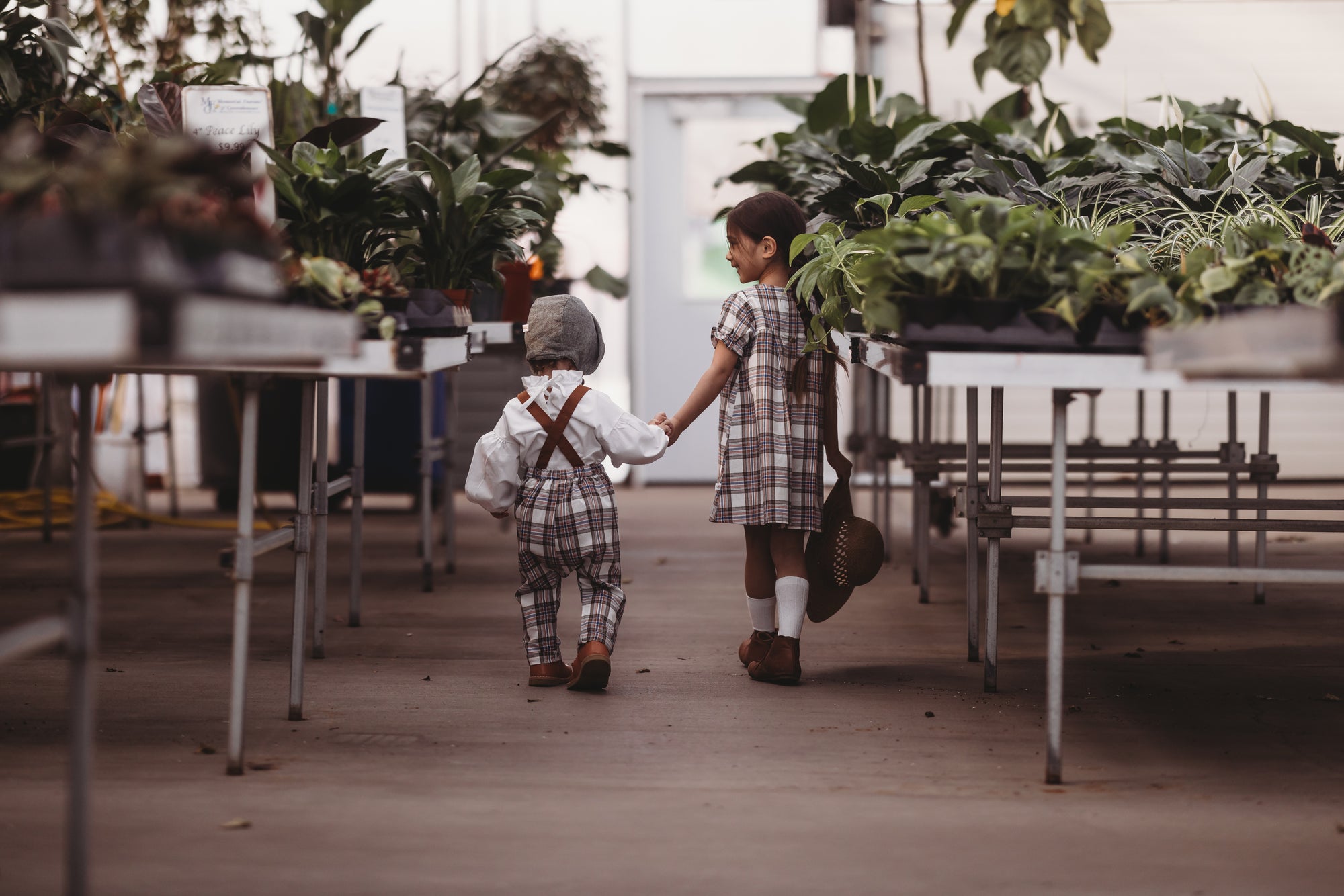 Two children holding hands in a greenhouse filled with plants.