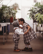 Two children in plaid outfits standing close together in a greenhouse.