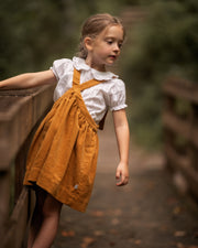 Young girl in a yellow dress with a white shirt standing on a wooden bridge.