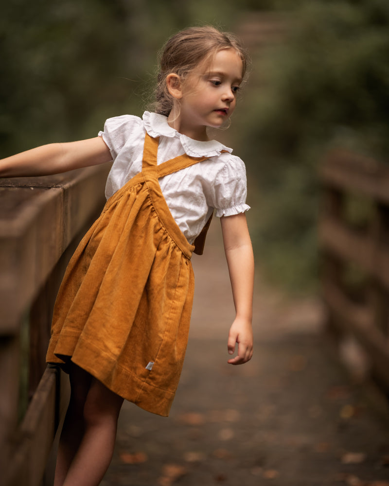 Young girl in a yellow dress with a white shirt standing on a wooden bridge.