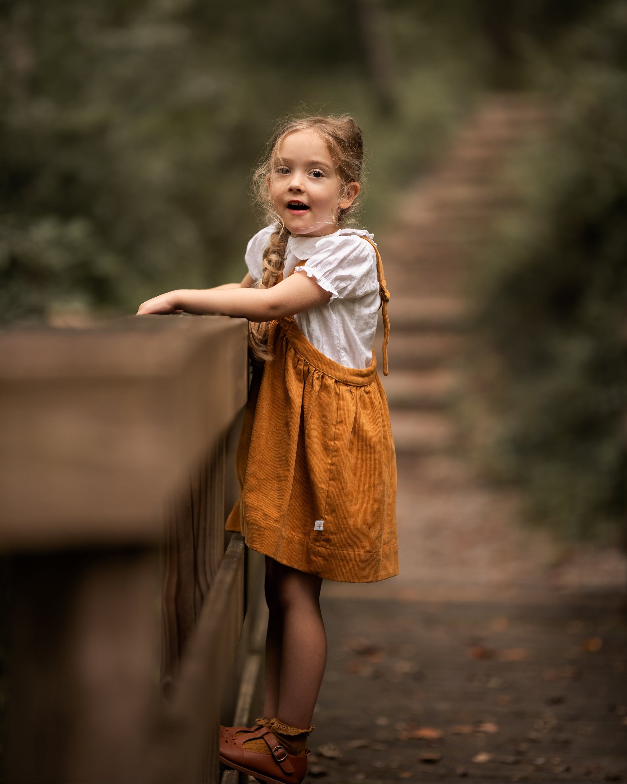 Young girl in a yellow dress standing on a wooden bridge with a forest background