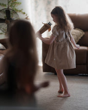 Young girl in a beige dress playing with a toy in a living room.