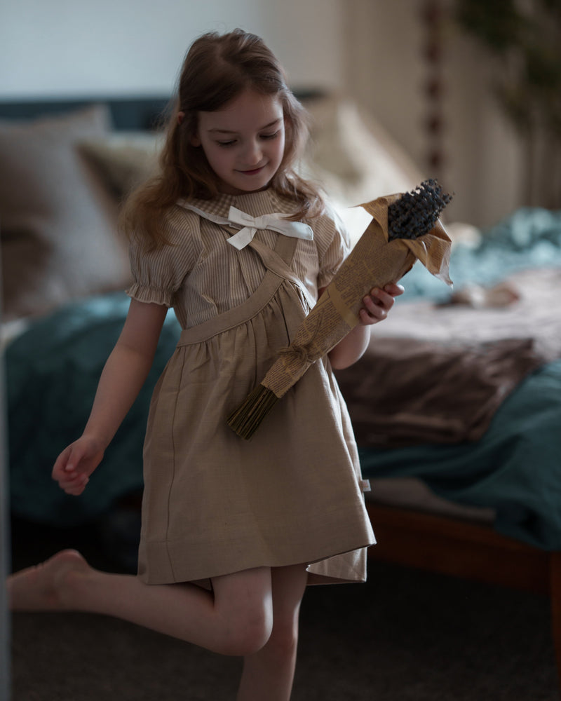 Young girl in a beige dress holding a toy broom in a bedroom setting