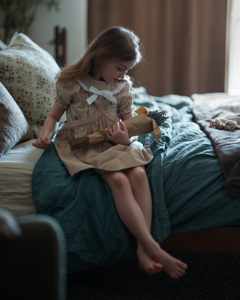 Young girl sitting on a bed holding a toy in a bedroom setting