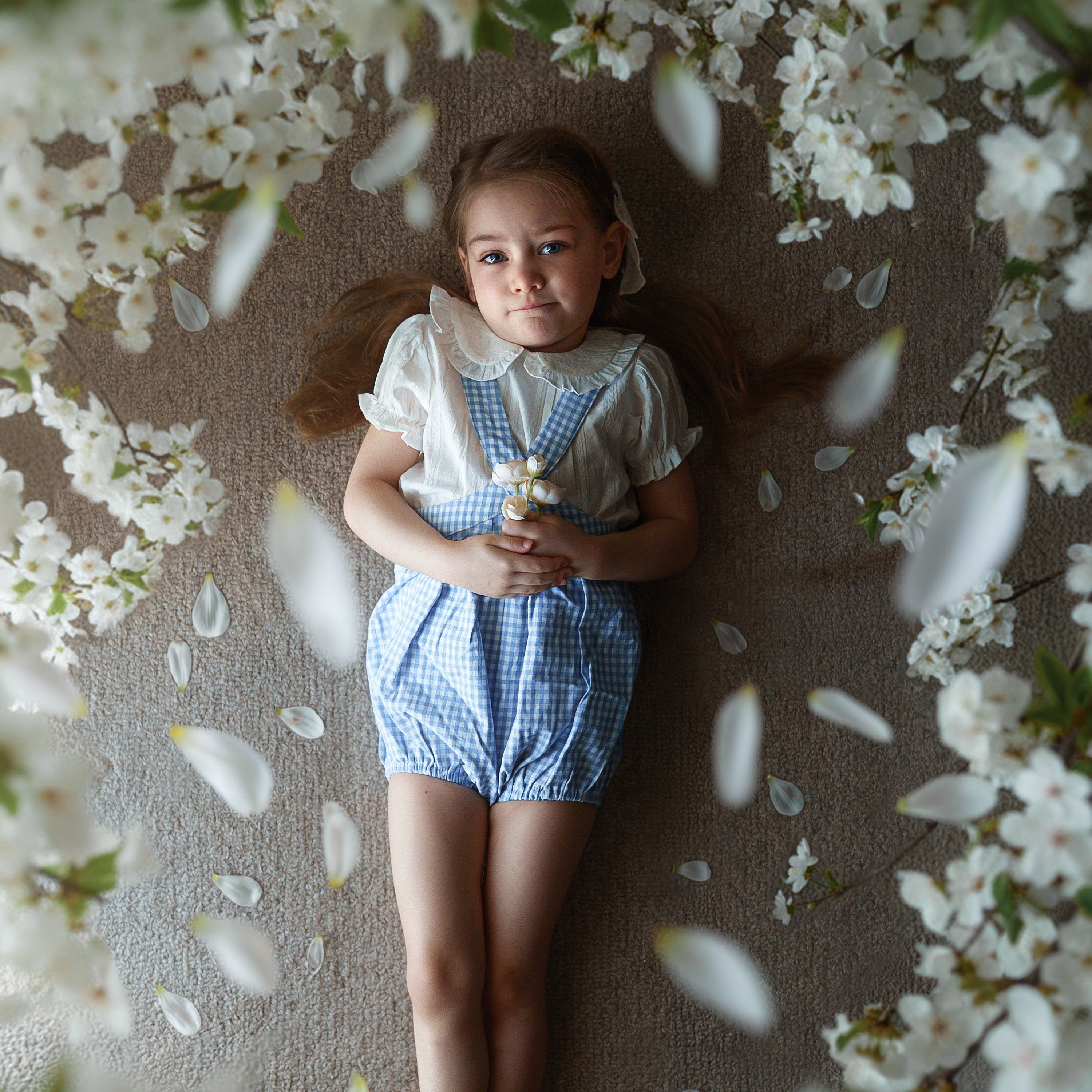 Young girl lying on a carpet with white flowers and petals around her