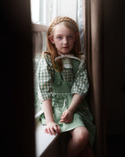 Young girl in a green dress sitting by a window