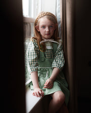 Young girl in a green dress sitting by a window
