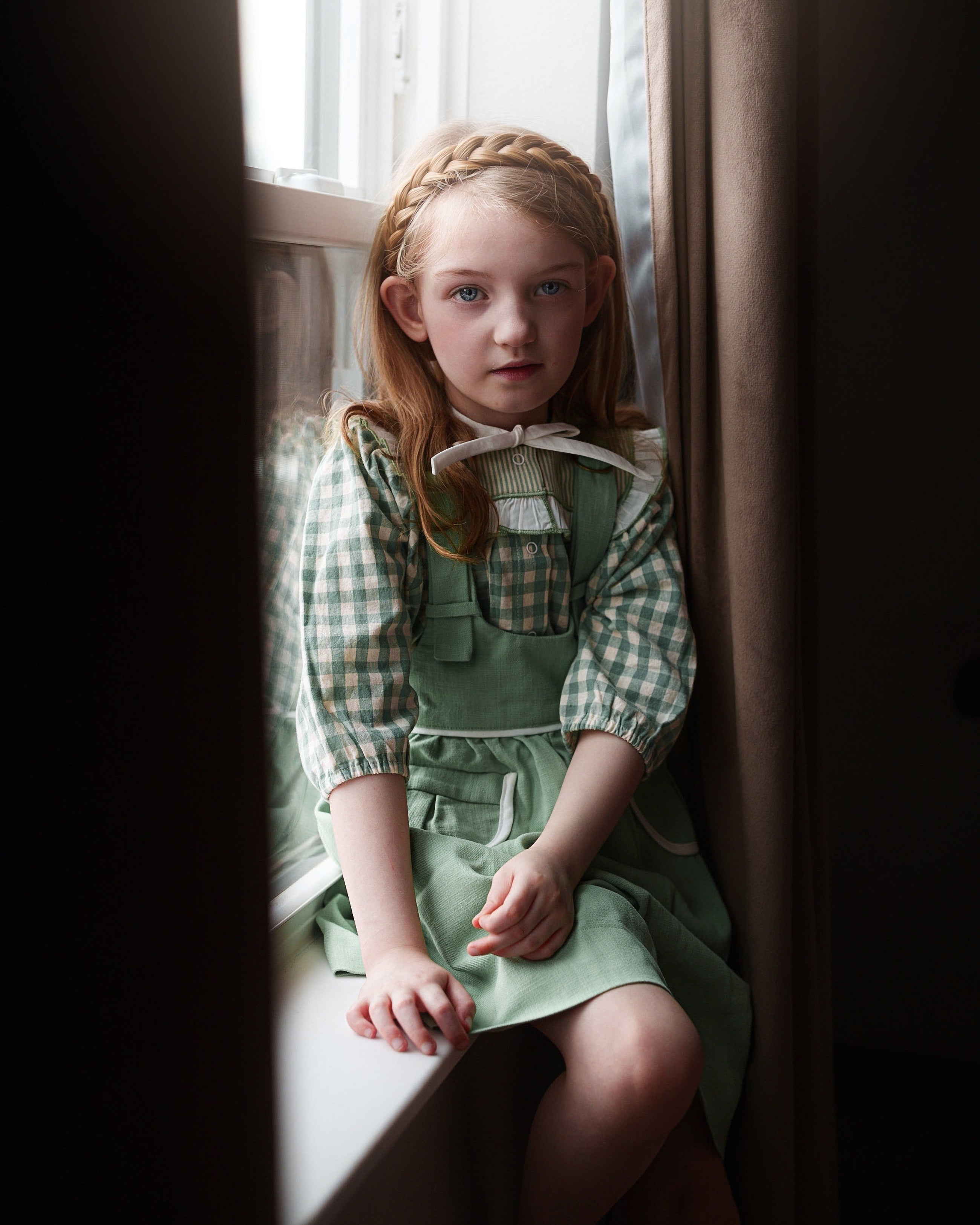 Young girl in a green dress sitting by a window