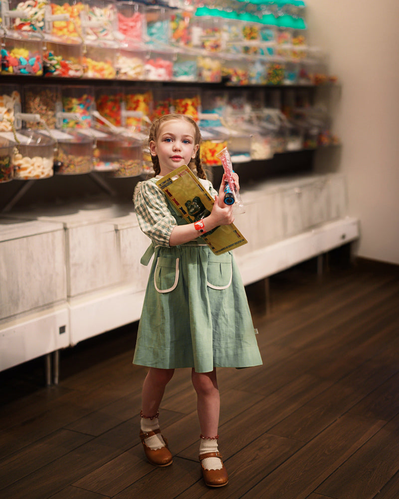 Young girl in a candy store holding a book and lollipop.