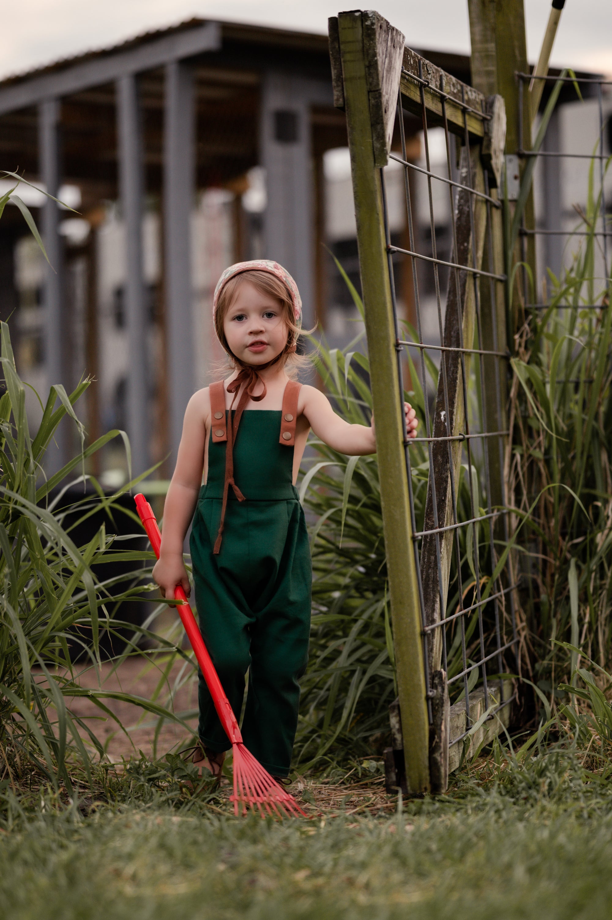 Full view of a 3-year-old girl working in the garden while wearing evergreen linen long overalls, emphasizing the breathable fabric and practicality for outdoor activities.