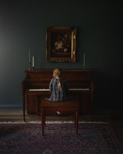 Person sitting at a piano in a dimly lit room with a painting on the wall.