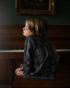 Child sitting on a piano bench in front of an upright piano with a dark, moody atmosphere.