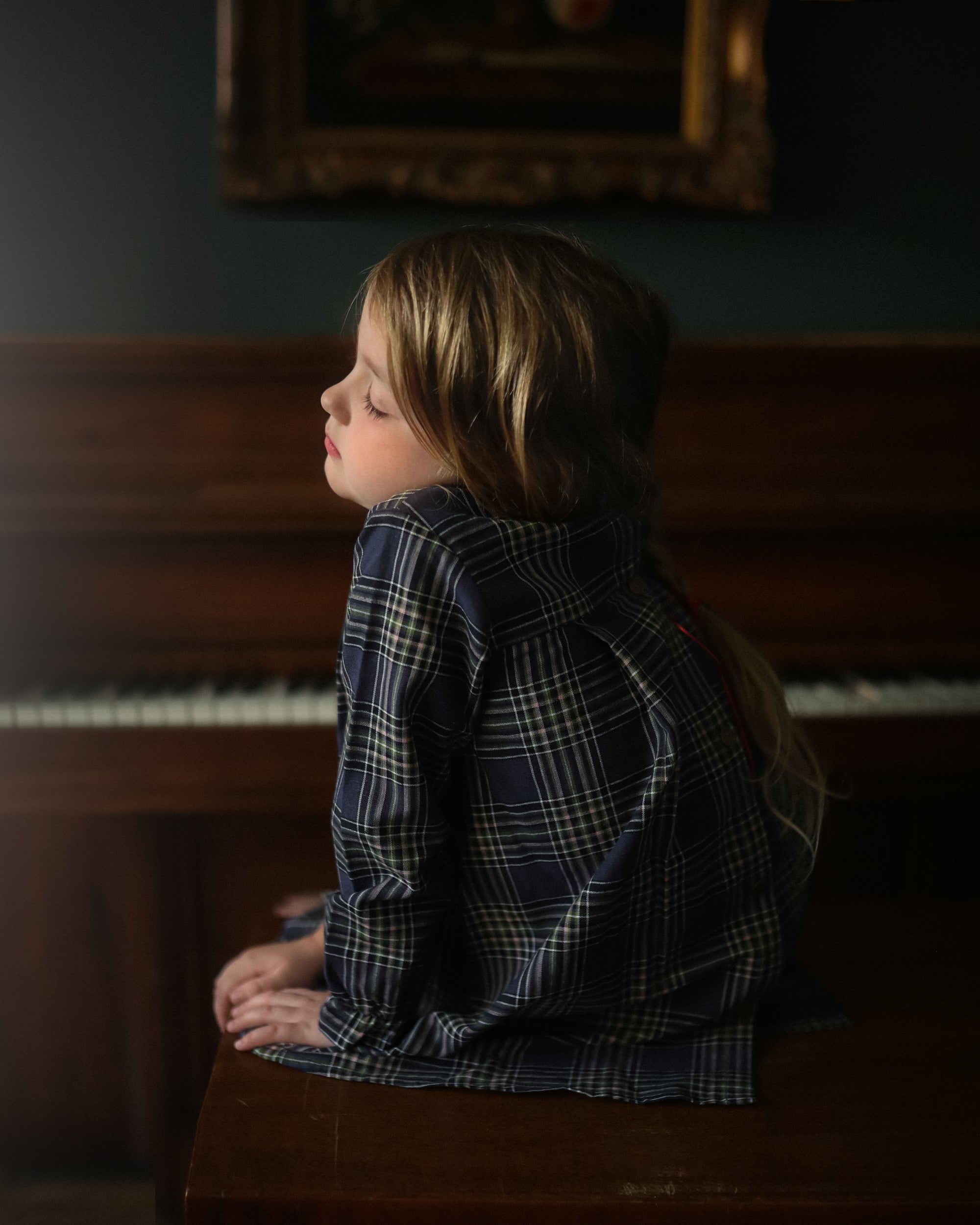 Child sitting on a piano bench in front of an upright piano with a dark, moody atmosphere.