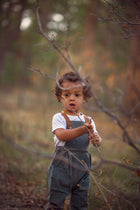 Child in overalls standing in a forest with blurred background